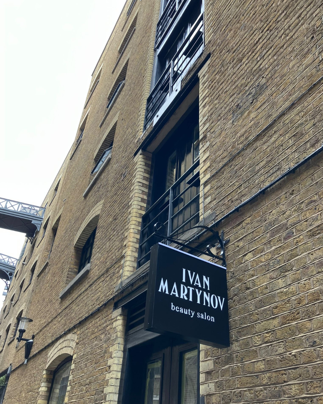 A building with a black hanging sign that says Ivan Martynov Beauty Salon